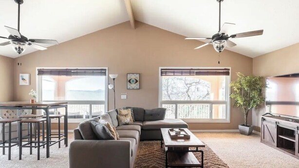 A spacious living room with a large sectional sofa, a coffee table, and a dining area with a table and chairs. There are two windows providing natural light and a view of the outdoors. - Explore natures retreat with amazing views of Lake Tulloch and close to Yosemite (Copperopolis)