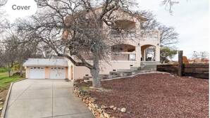 A two-story house with a covered driveway, a stone retaining wall, and a large tree in front. - Explore natures retreat with amazing views of Lake Tulloch and close to Yosemite (Copperopolis)