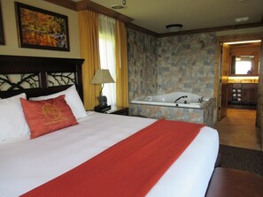 Ein Hotelzimmer mit einem großen Bett, einem Bild an der Wand, einem Badezimmer mit einer Badewanne und Blick auf den Flur.