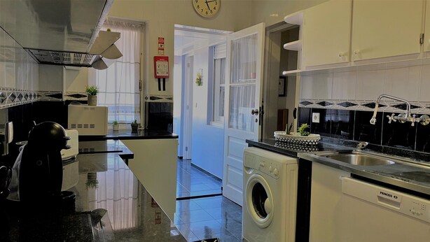 A kitchen with a washing machine, a sink, and a clock on the wall.