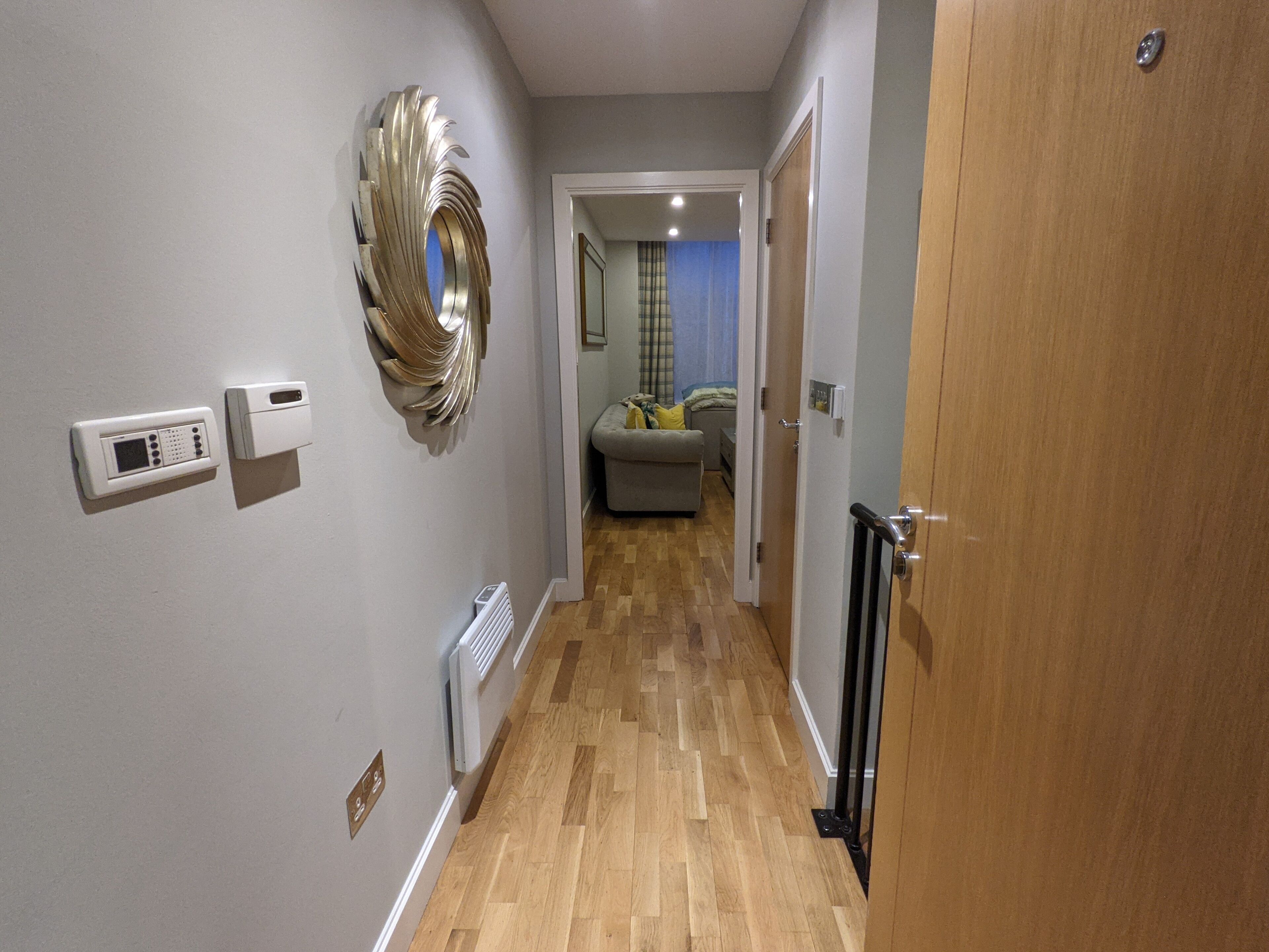 A hallway with a radiator, a wall-mounted thermostat, and a decorative mirror.