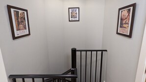 En smal trapphall med svarta räcken och tre inramade affischer på väggarna.