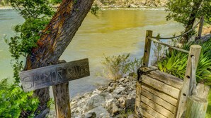 A wooden staircase leading down to a river, surrounded by greenery and a mountainous backdrop.
