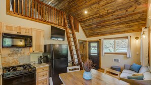 A kitchen with wooden cabinets, a stove, a refrigerator, a microwave, and a wooden staircase to an upper level.