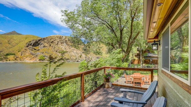 A wooden deck with outdoor seating, overlooking a river and hills.