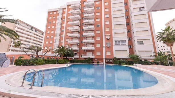 A multi-story residential building with balconies, a swimming pool, and palm trees. - Apartamentos Marblau Las Alondras (Gandia)