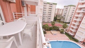 A balcony with a white table and chairs, overlooking a swimming pool and adjacent buildings. - Apartamentos Marblau Las Alondras (Gandia)