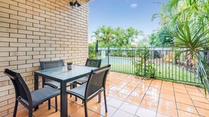 A patio with a table and chairs, a potted plant, and a view of a garden with palm trees. - Between Hastings Street and Noosa Junction (Noosa Heads)