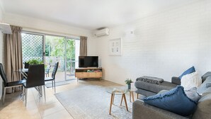 Een moderne woonkamer met een televisie, bank en eethoek.