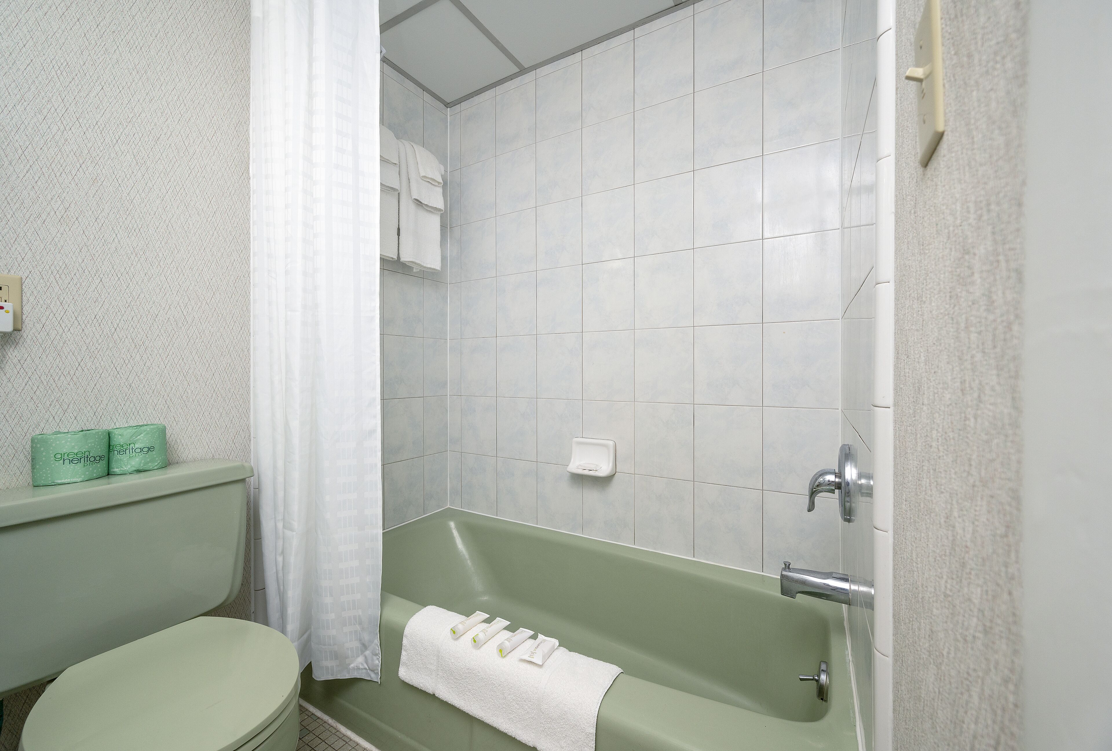 A bathroom with a green bathtub, white toilet, and a shower curtain.