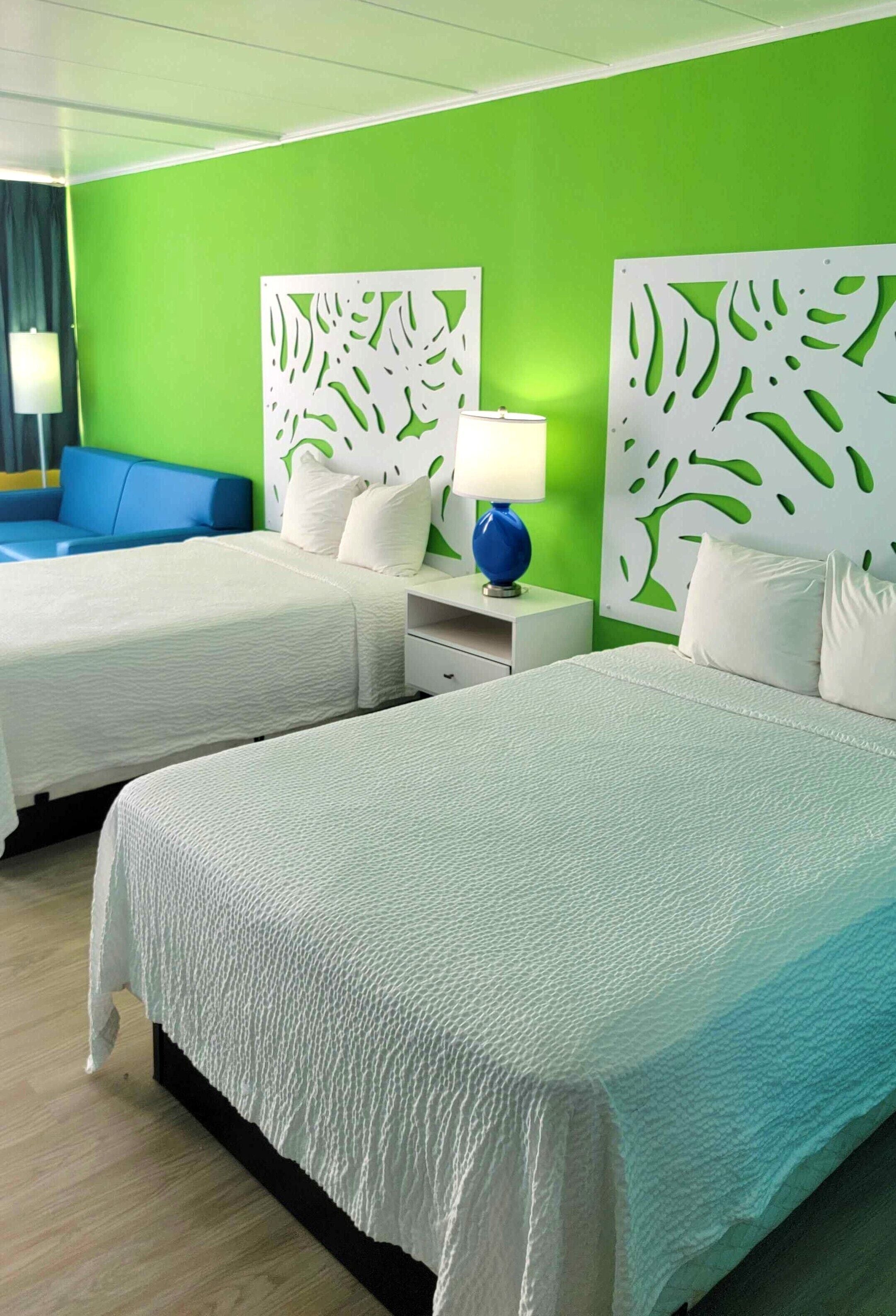 Une chambre d’hôtel avec deux lits, un canapé bleu et un mur d’accent vert.