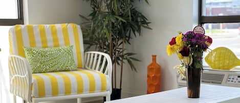 A room with a white striped chair, a small table, a blue patterned rug, a potted plant, and a window with a view.