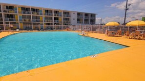 Una piscina con un borde amarillo, rodeada por una valla blanca y un edificio con balcones.
