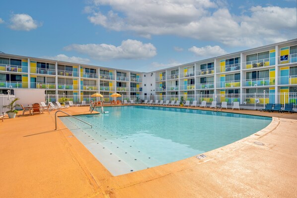 Un hotel de varios pisos con piscina, mobiliario exterior y balcones.