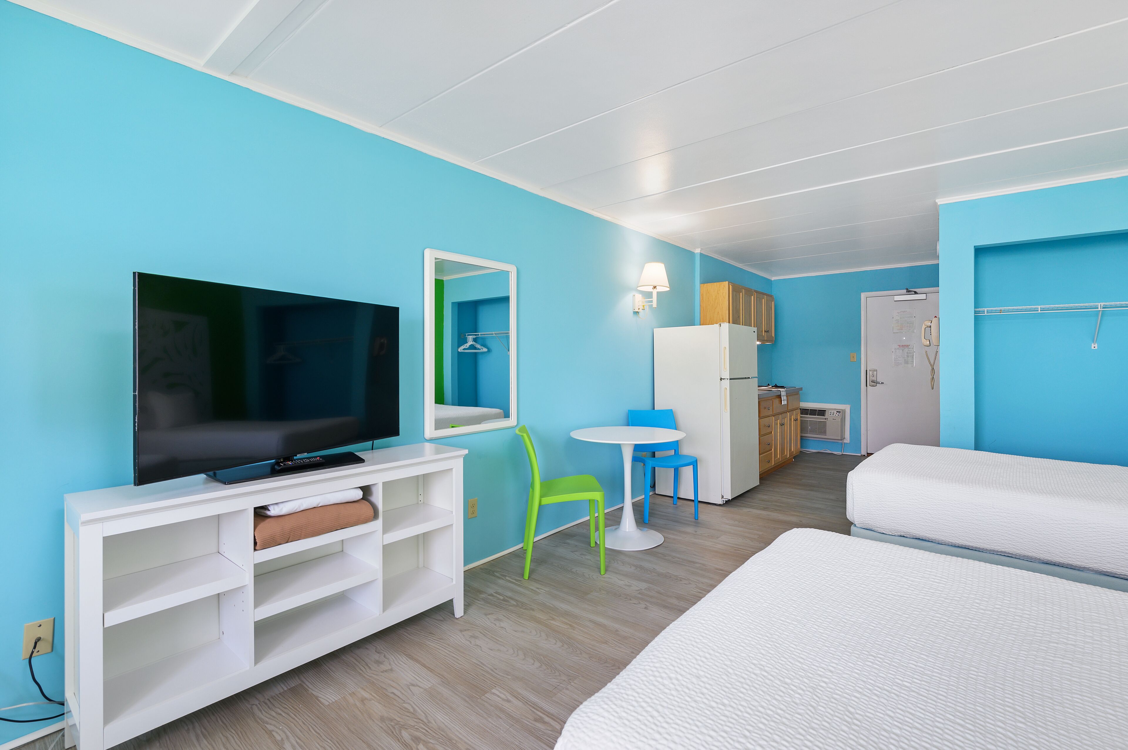 Ett hotellrum med en TV, ett litet bord, två stolar, en säng och ett minikylskåp.
