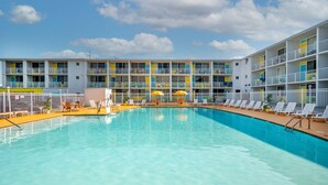 Piscina com espreguiçadeiras e guarda-sóis, cercada por edifícios com varandas.