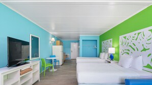 Quarto de hotel com cama, televisão, secretária com cadeira e uma pequena cozinha.