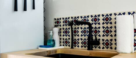 Uma cozinha com bancada de madeira, uma torneira preta e uma pia. Há um dispensador de sabonete e uma toalha na bancada.
