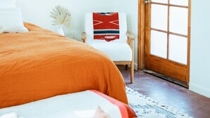 Un dormitorio con una cama grande, una puerta de madera, una silla blanca y una mesita con un florero.