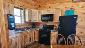 Cocina tipo cabaña de madera con estufa, microondas, refrigerador y armarios de madera.