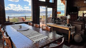 A rustic interior with a large wooden dining table, leather chairs, a fireplace, and a scenic mountain view through large windows. - NO BETTER VIEW THAN THIS (Island Park)