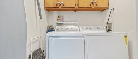 A laundry area with a washer and dryer, wooden cabinets above, and a metal rack with a laundry detergent box.