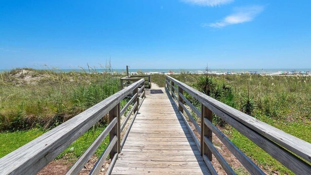 Une promenade en bois menant à une plage, avec un ciel dégagé.