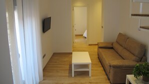 Un salon comprenant un canapé, une table basse, un téléviseur fixé au mur et un escalier menant à une autre pièce.
