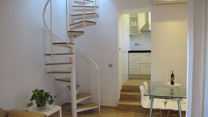 Un intérieur moderne avec un escalier en colimaçon, un coin repas doté d’une table en verre et une cuisine en arrière-plan.
