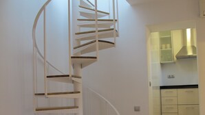 Un intérieur moderne avec un escalier en colimaçon, une petite table agrémentée d’une plante et une vue sur un espace cuisine.