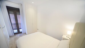 Une chambre à coucher avec un lit, une table de chevet avec une lampe, une porte avec une fenêtre et un interrupteur sur le mur.