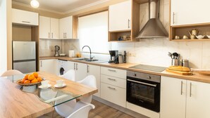 A modern kitchen with white cabinets, a glass dining table, and a stainless steel range hood. - Entheos City Center (Argostoli)