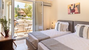 A hotel room with two beds, a balcony with a table and chairs, and a painting on the wall. - Entheos City Center (Argostoli)
