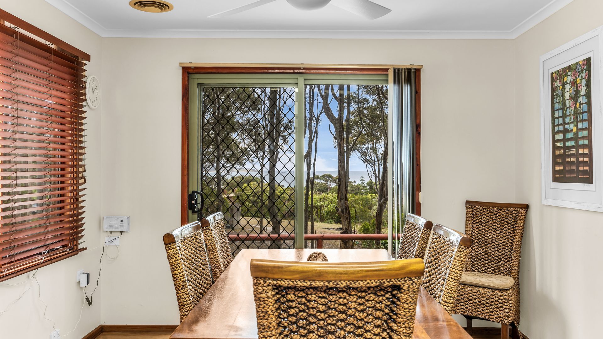 A dining area with a table and chairs, a view through a window with a metal grid, and a ceiling fan.