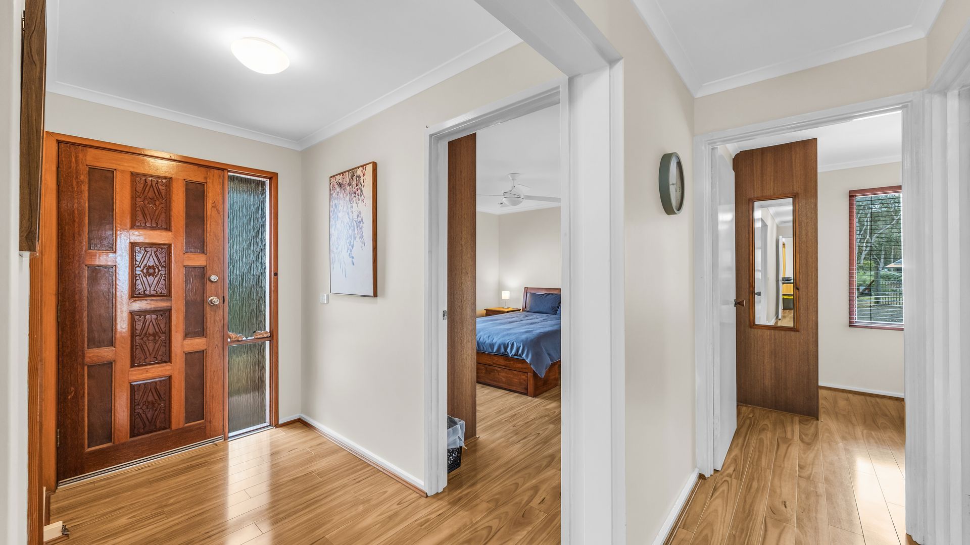 A hallway with wooden flooring, a wooden door with glass panels, and a bedroom visible through an open door.