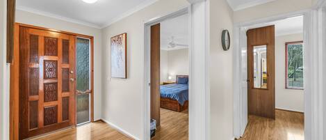 A hallway with wooden flooring, a wooden door with glass panels, and a bedroom visible through an open door.