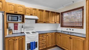 A kitchen with wooden cabinets, a microwave, stove, and a window with blinds.