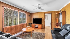 A living room with a television, wooden furniture, and a ceiling fan.