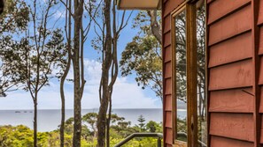 A wooden exterior wall with a window, overlooking a coastal landscape with trees and the sea. - Bush & Beach Retreat - Amaroo Avenue 7 (BARRAGGA BAY)