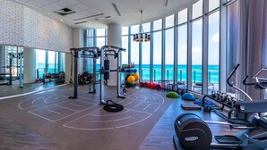 Un gimnasio con vistas al océano, equipamiento para levantamiento de pesas y máquinas de cardio.