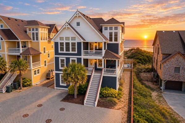 A multi-story residential building with a balcony, a staircase, and a view of the ocean at sunset.