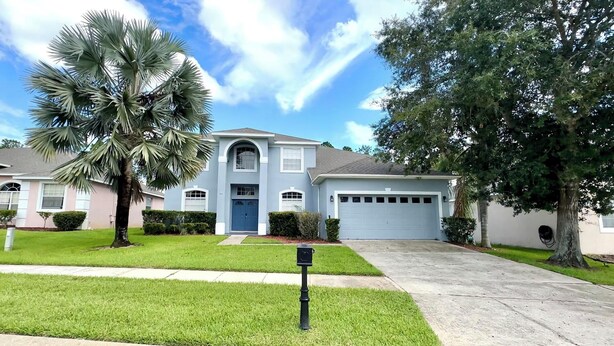 A two-story house with a blue front door, a garage, and a well-maintained lawn. - Modern and Well Equipped 6/3 Pool Home on Golf Community. Perfectly accommodating for families with ample space inside and out! (Davenport)