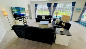 A living room with a black sofa, a coffee table, a TV, and a lamp. - Modern and Well Equipped 6/3 Pool Home on Golf Community. Perfectly accommodating for families with ample space inside and out! (Davenport)