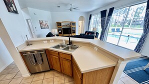 A modern kitchen with a built-in dishwasher, wooden cabinets, and a large window offering a view of the outdoors. - Modern and Well Equipped 6/3 Pool Home on Golf Community. Perfectly accommodating for families with ample space inside and out! (Davenport)
