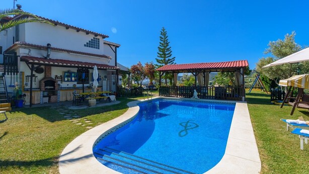 A swimming pool with a tiled deck, a covered seating area, and a house with a tiled roof and outdoor kitchen. - Finca El Albero Carratraca by Ruralidays (Málaga)