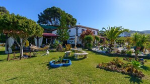 A well-maintained garden with outdoor seating, a white building with a red roof, and a clear blue sky. - Finca El Albero Carratraca by Ruralidays (Málaga)