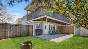 Une maison à deux étages avec un patio couvert, une clôture en bois et un barbecue.