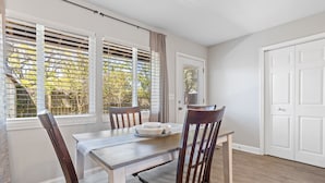 Un coin repas avec une table et des chaises en bois, une fenêtre avec des stores et une porte.