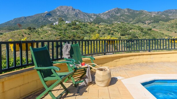 Zona de piscina amb caires i taula, amb vista a un paisatge de muntanyes.
