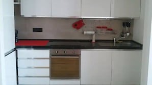 Una cocina compacta con armarios blancos, horno de acero inoxidable y encimera negra.